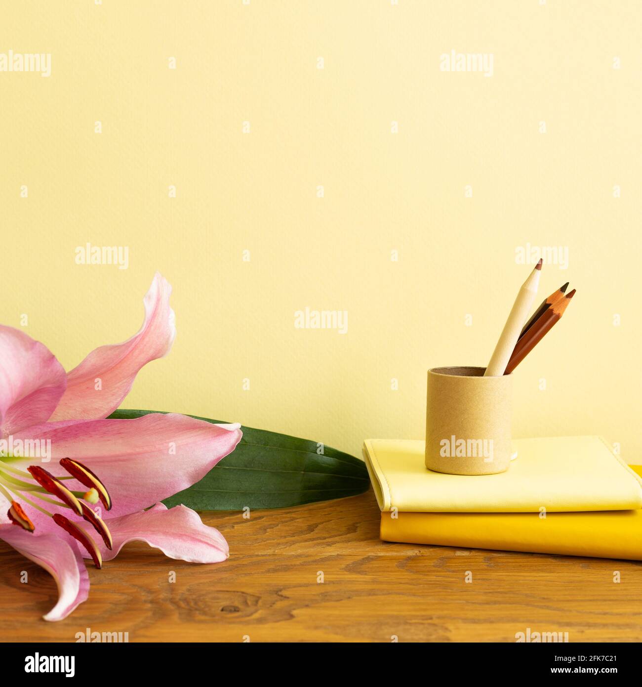Notizbuch, Buntstifte, Blume auf Holzschreibtisch. Gelber Hintergrund. Arbeits- und Studienort Stockfoto