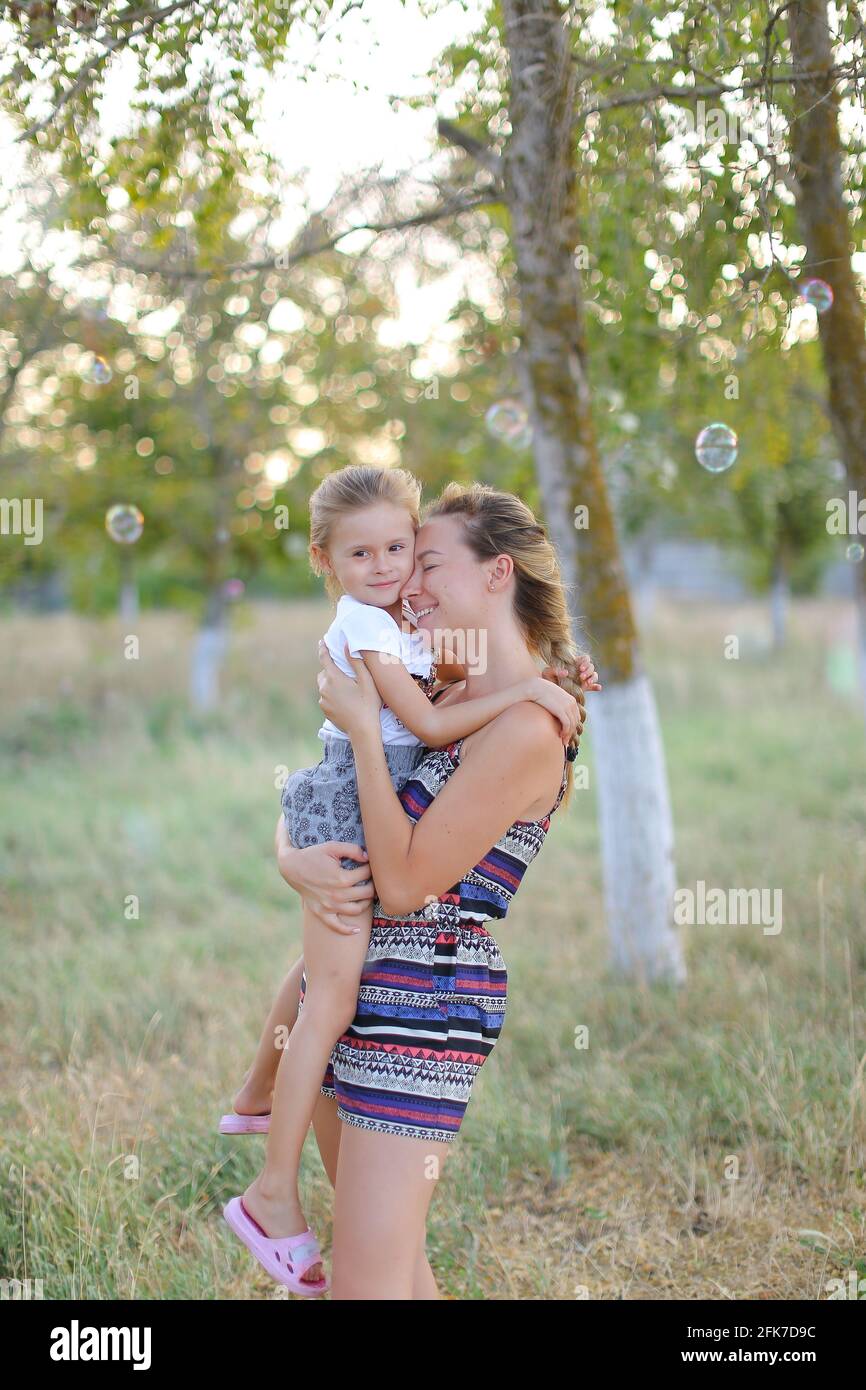 Junge Frau hält Tochter im Park, Seife bläserte im Hintergrund. Stockfoto