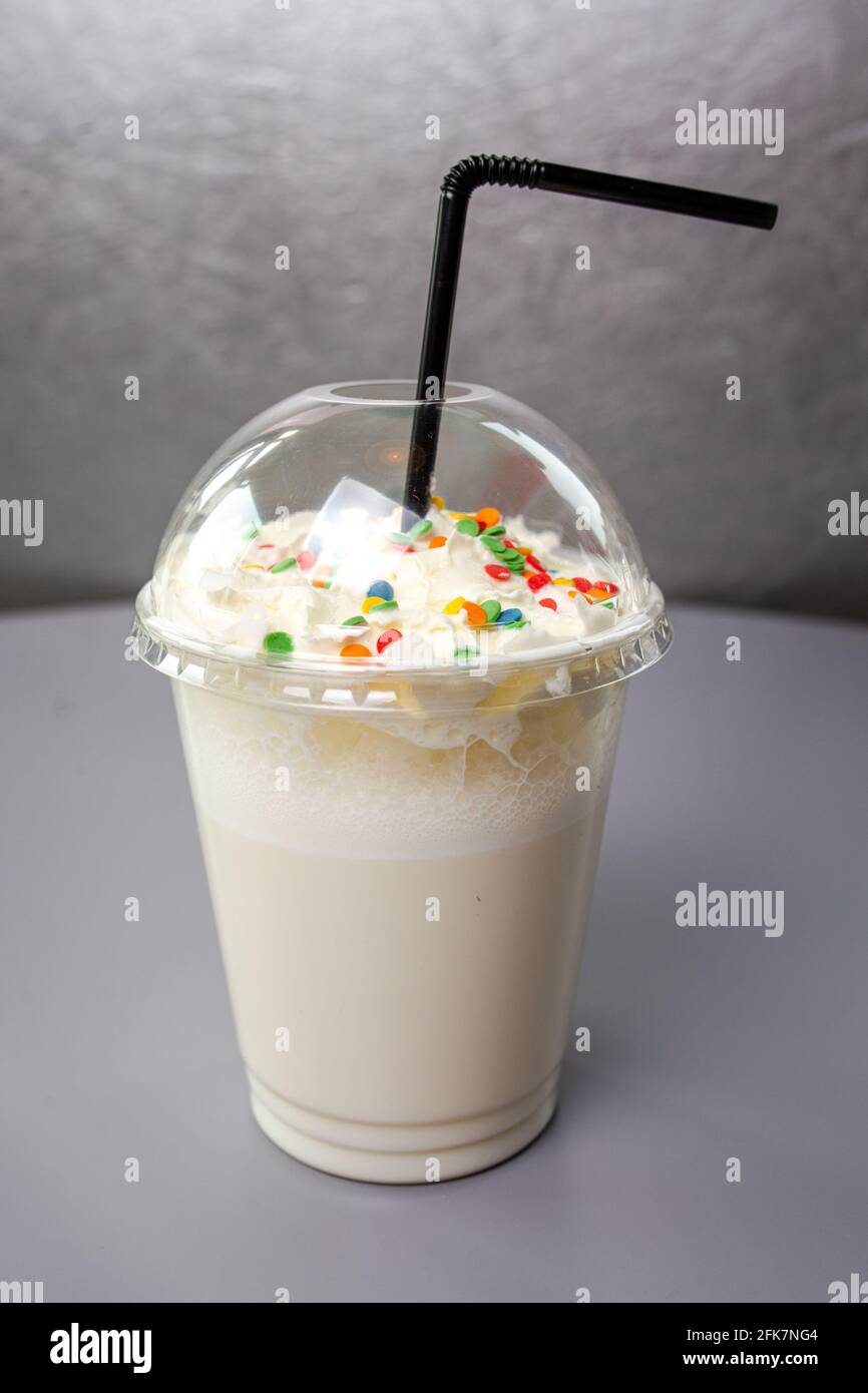 Süßer Milchcocktail in einem Plastikglas mit schwarzer Knolle. Stockfoto