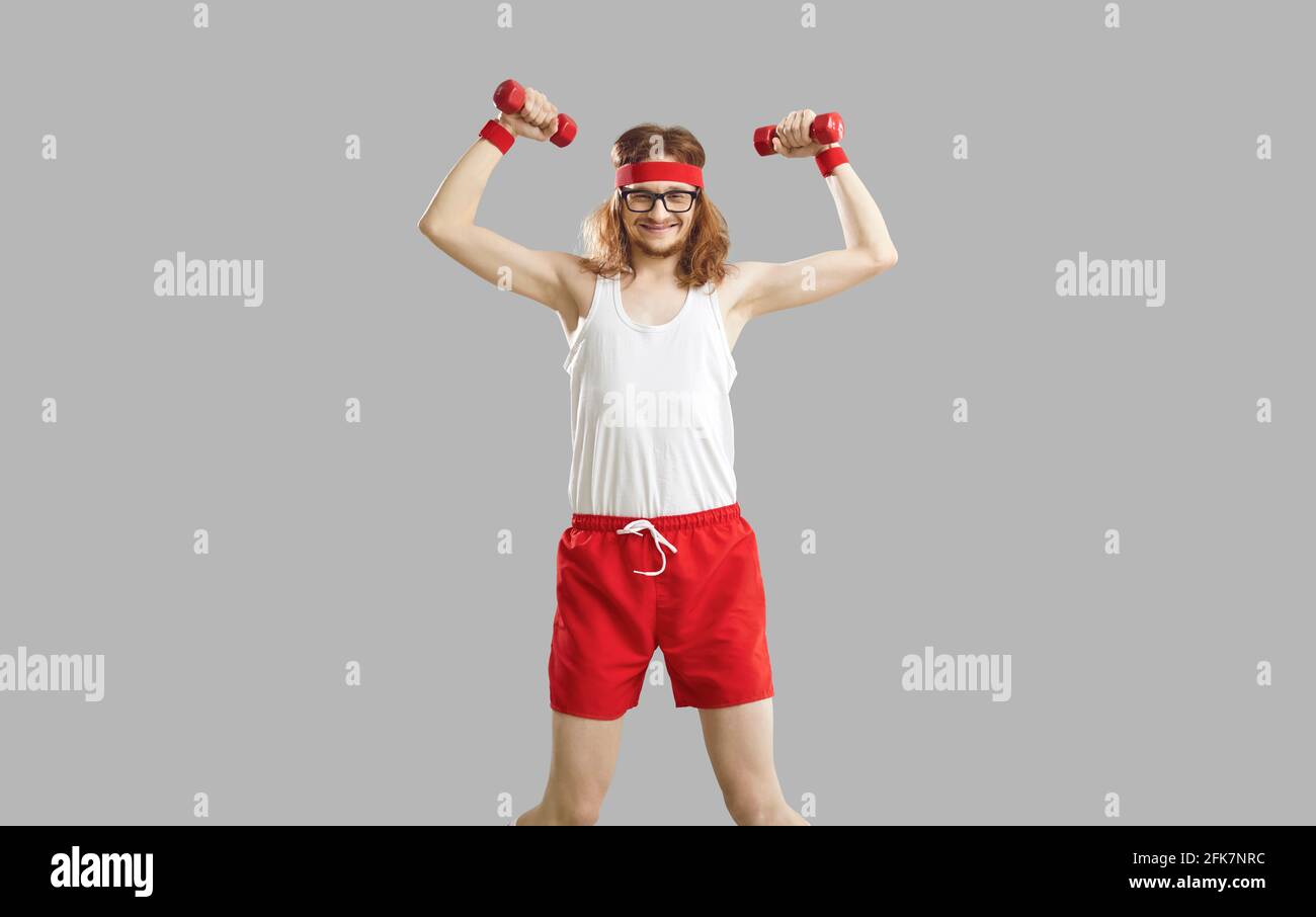 Lustige dünne Mann mit Hanteln trainieren schwache Muskeln isoliert auf Grauer Hintergrund Stockfoto