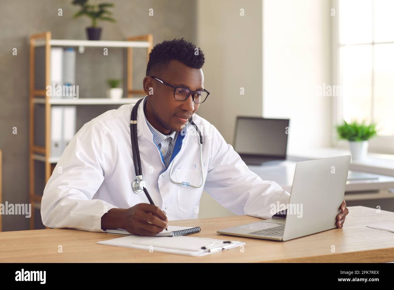 Arzt Arzt Arzt Blick auf Laptop-Bildschirm und Schreiben von Notizen Auf Papier Stockfoto