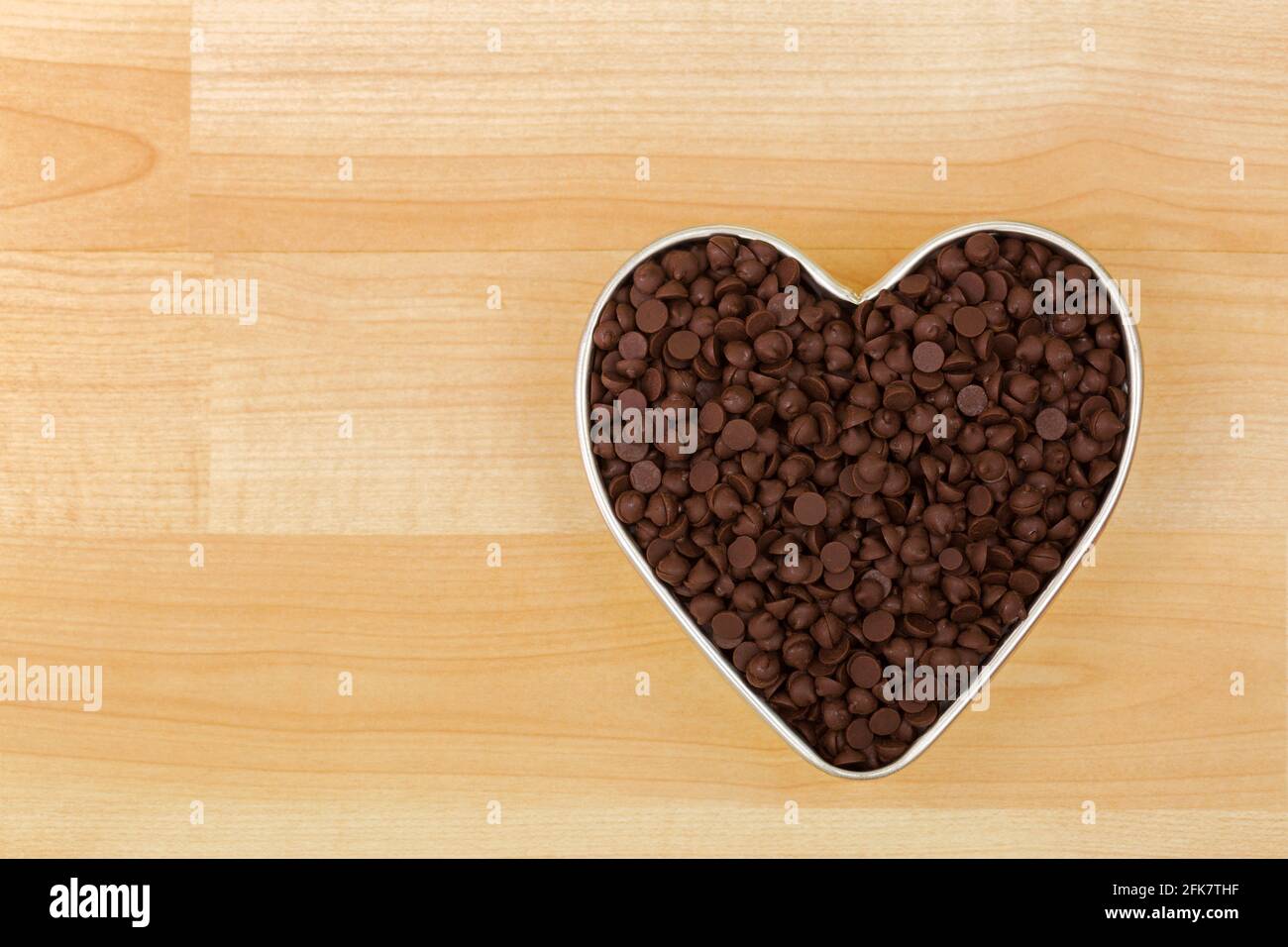 Kleine Stücke von gesüßten Schokoladenstückchen in herzförmiger Dose Schüssel auf Holzhintergrund mit Copyspace Stockfoto