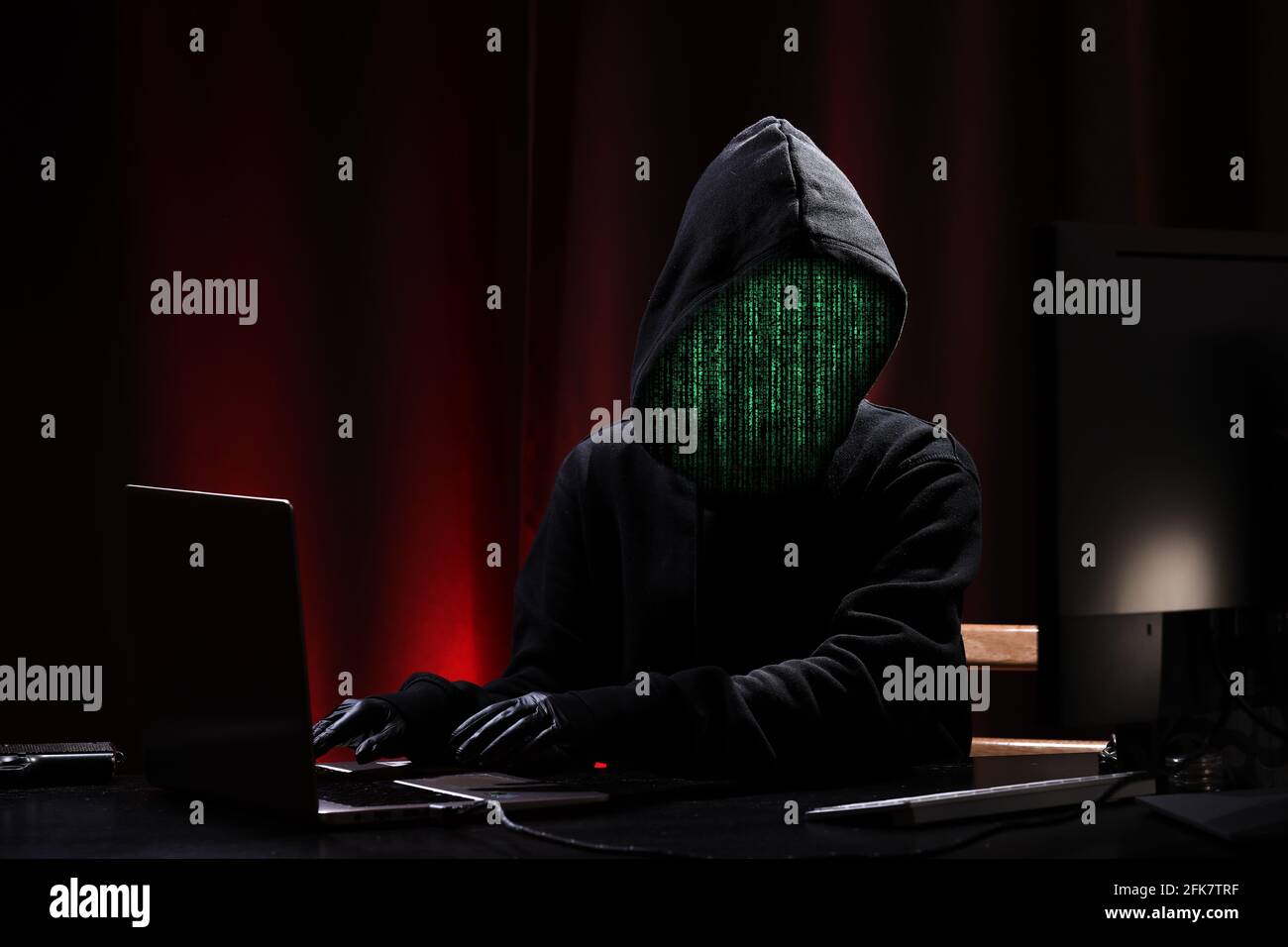 Internationaler Hacker in schwarzem Pullover und schwarzer Maske versucht, die Regierung auf schwarzem und rotem Hintergrund zu hacken. Cyberkriminalität . Cyber-Sicherheit. Matrixeffekt Stockfoto