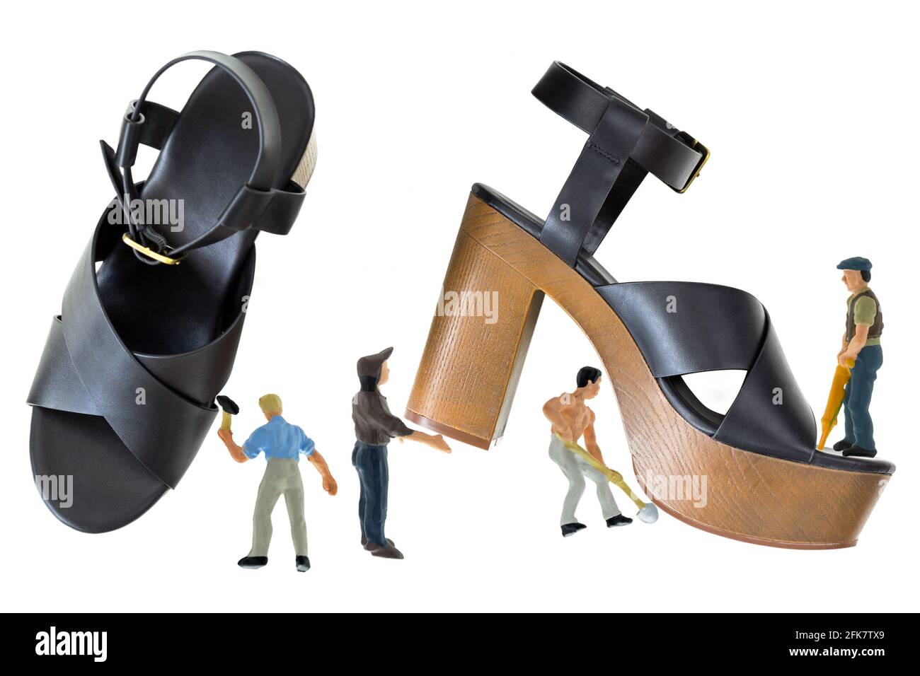 Mini-Männer arbeiten an schwarzen High-Heel-Schuhen mit offenem Zehenbereich und überkreuztem Riemen, Plattform-Sandalen mit braunem Blockabsatz, Knöchelriemen wird mit Metallbuck befestigt Stockfoto