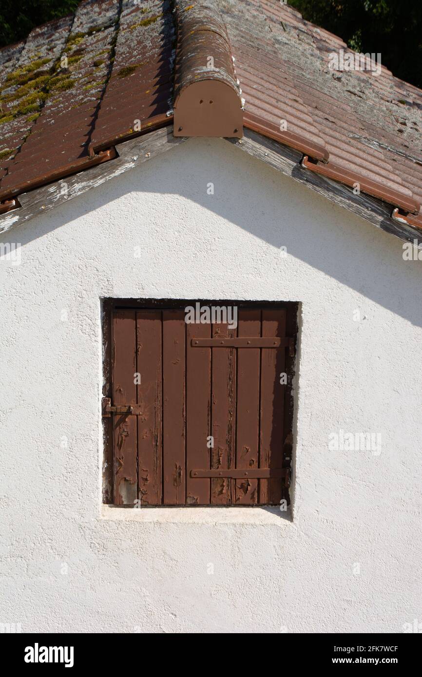 Geschlossene braune hölzerne Fensterluke auf einer weißen Fassade Ein kleines Haus Stockfoto