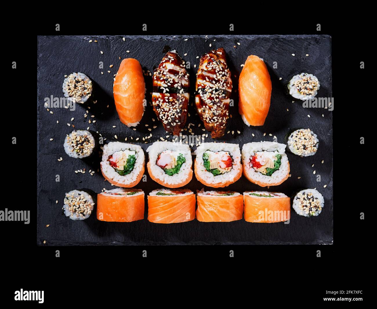 Draufsicht auf köstliches Sushi mit Rollen aus Kalifornien, Sashimi und Maki auf einem schwarzen Teller. Japanische orientalische Küche mit rohem Fisch, Käse, Sesam Stockfoto