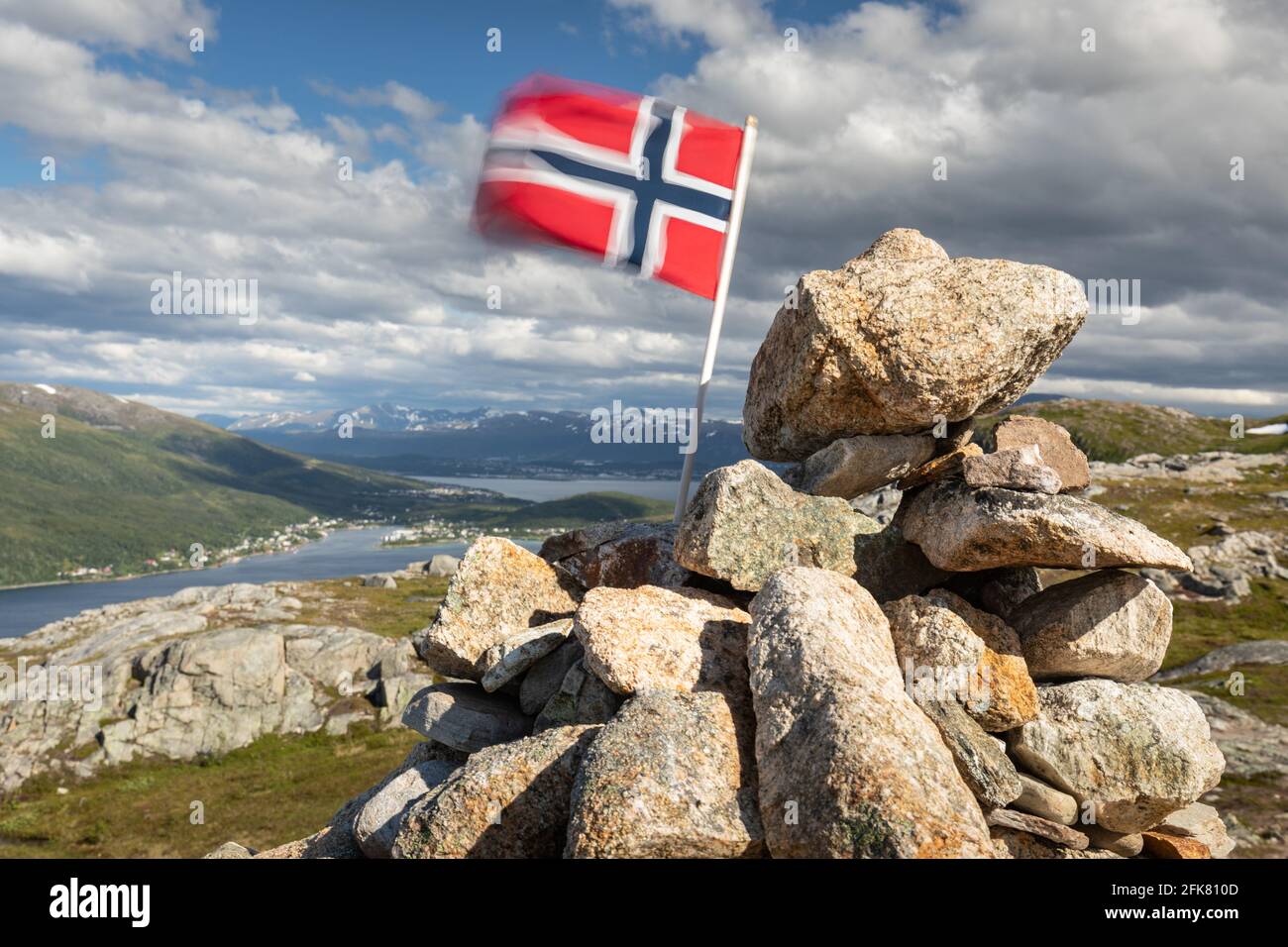 Norwegische Flagge im Wind auf den Bergen oben. Felsen, Fjord, Stadt Tromso und verschneite Berge im Hintergrund Stockfoto