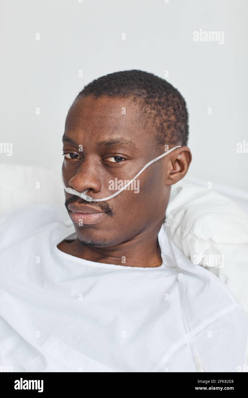 Vertikales Nahaufnahme-Porträt eines afroamerikanischen Mannes, der im Krankenhausbett liegt Mit Sauerstoff-Stützröhrchen und Blick auf die Kamera Stockfoto