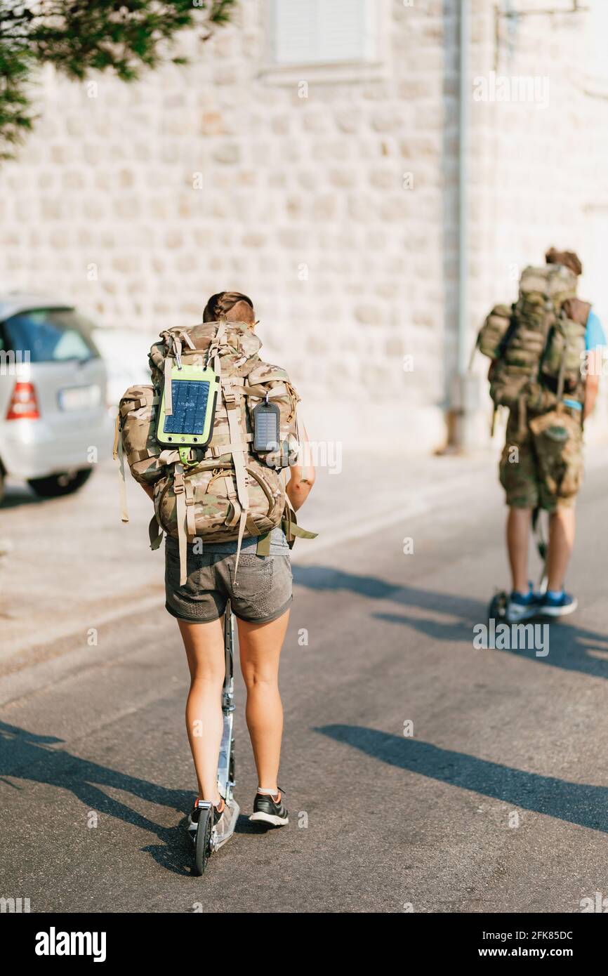 Ein paar Touristen reisen mit Motorrollern durch Europa. Zwei Reisende fahren mit Touristenrucksäcken und Sonnenkollektoren die Straße entlang. Stockfoto