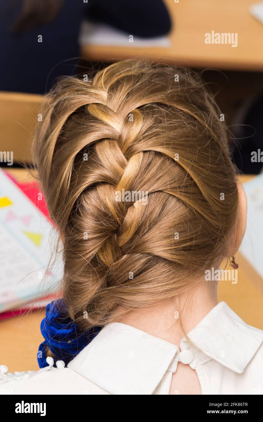 Die Frisur eines Mädchens ist in einem Flechtband mit einem blauen Gummiband  aus der Nähe geflochten. Das Styling der Haare erfolgt mit Haarnadeln und  einem elastischen Band. Nur der Hinterkopf mit einem