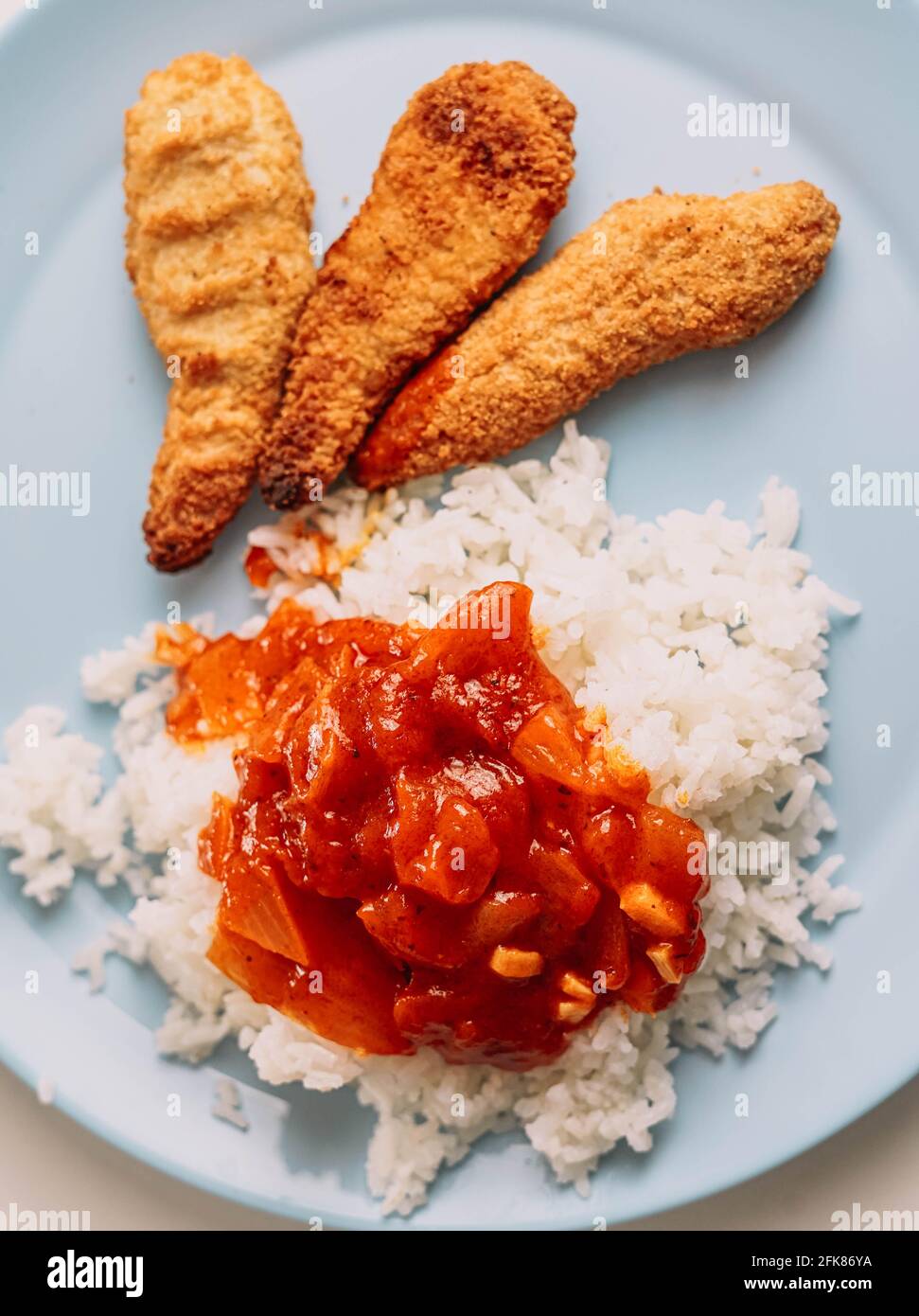Teller mit Kindermenü mit panierten Hähnchenstreifen und Reis Mit Tomatensauce Stockfoto