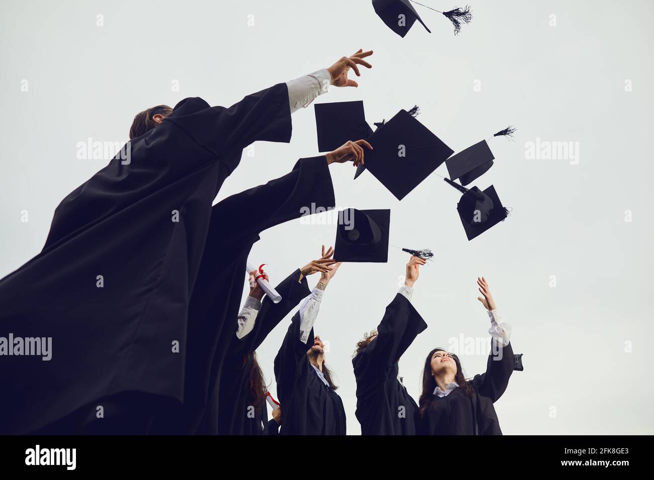 Absolventen werfen ihre akademischen Hüte während einer feierlichen Zeremonie an der Universität in den Himmel. Stockfoto