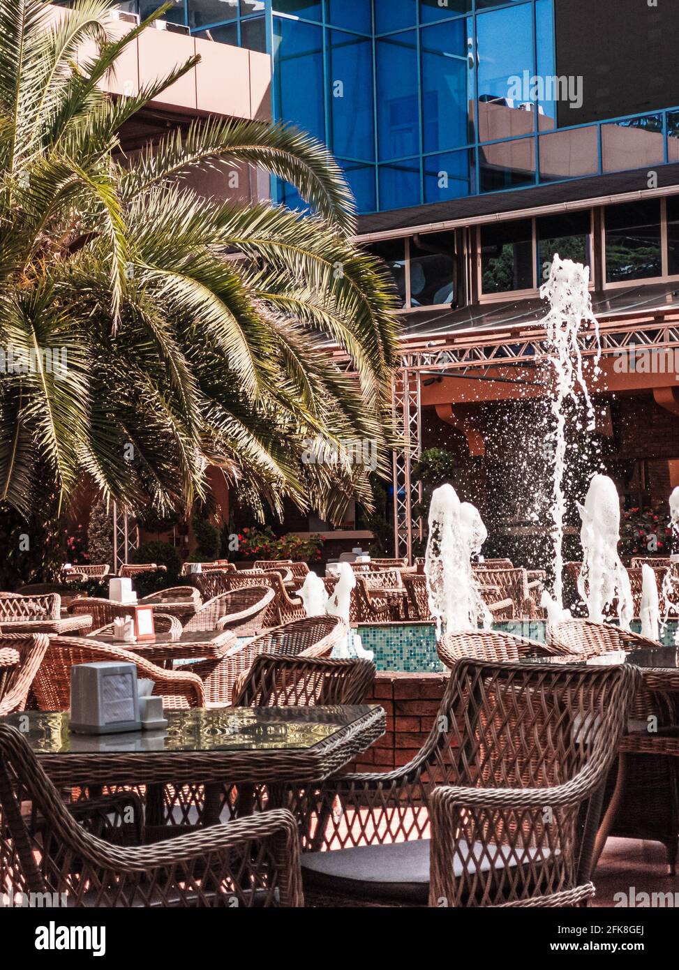 Leere Tische im Café oder Restaurant unter freiem Himmel mit Palmen und Springbrunnen. Straßencafé innen. Urlaubs- und Resort-Konzept. Vertikal. Stockfoto