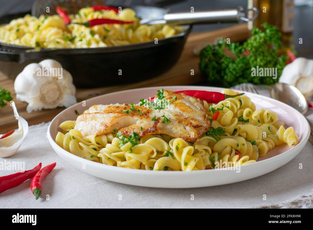 Gesundes italienisches Gericht mit Pasta aglio e olio und gebraten Fisch serviert auf dem Teller auf rustikalem Küchentisch Hintergrund Stockfoto