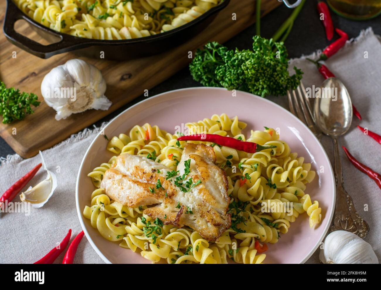 Gesundes italienisches Gericht mit Pasta aglio e olio und gebraten Fisch serviert auf dem Teller auf rustikalem Küchentisch Hintergrund aus Oben Stockfoto