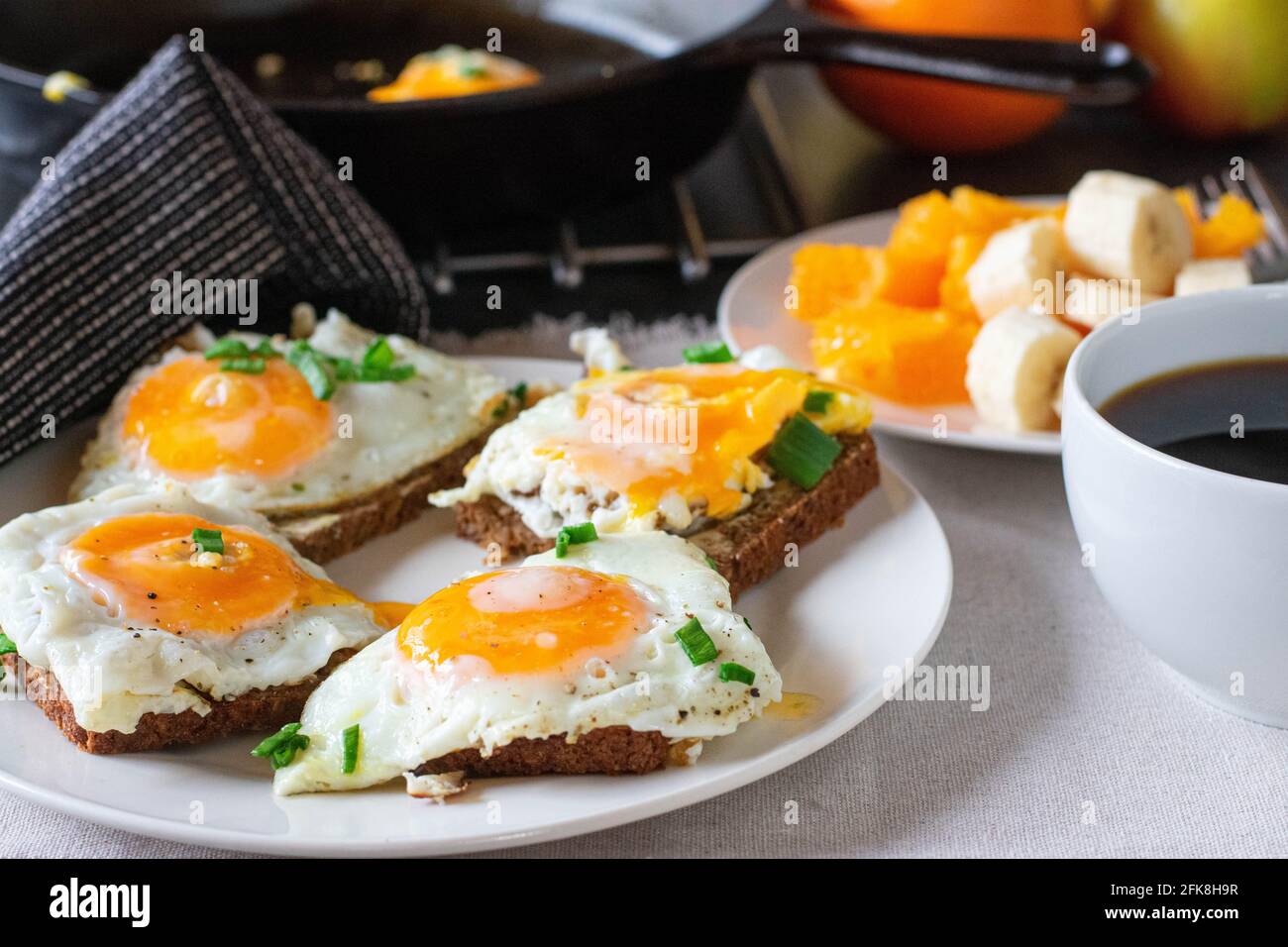 Stillleben eines herzhaften Frühstücks mit gebratenen Ei-Sandwiches, Kaffee und Obst auf einem Tisch mit verschwommenem Hintergrund serviert Stockfoto