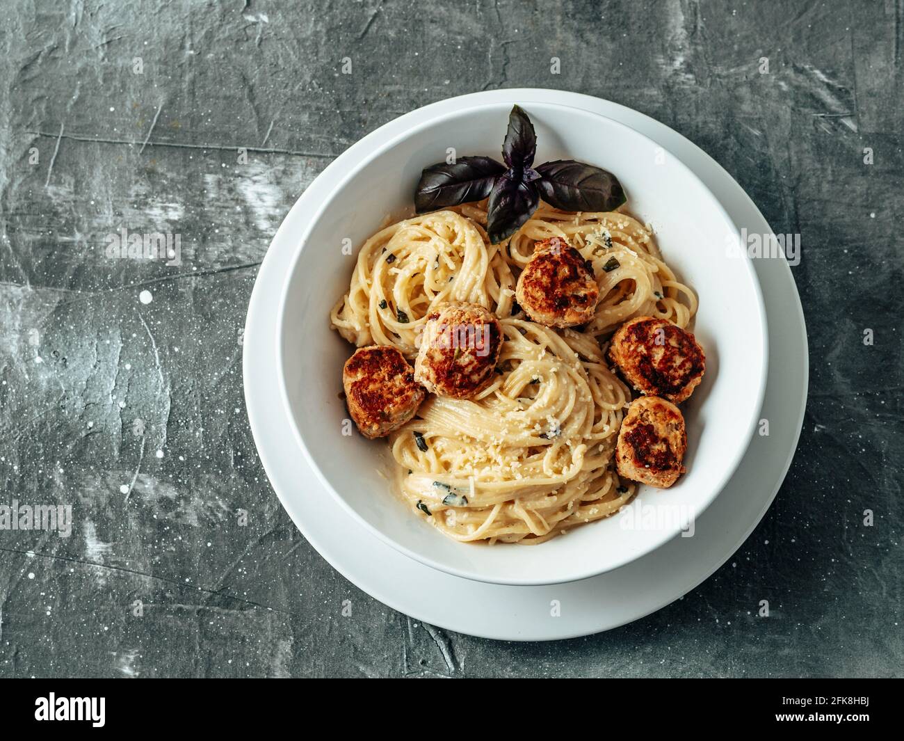 Zucchini Parmesan Fleischbällchen mit Pasta Carbonara in weißer Platte auf grauem Hintergrund. Nahaufnahme von cremigem Carbonara mit Kopieplatz links. Ansicht von oben oder flach liegend. Stockfoto