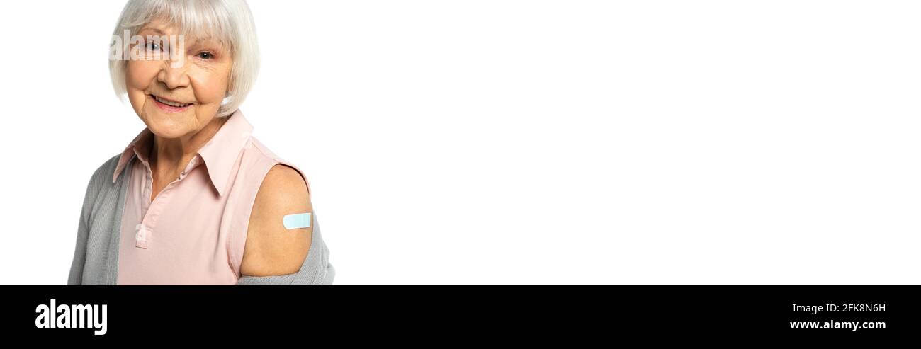 Glücklicher älterer Patient mit Klebstoff-Gips auf dem Arm, der die Kamera isoliert auf weißem Banner ansieht Stockfoto