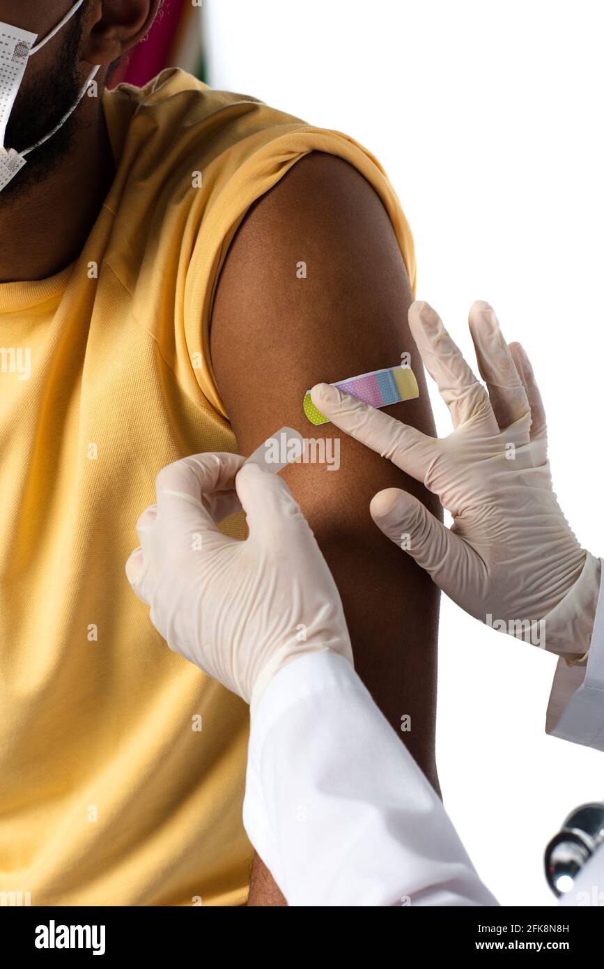 Beschnittene Ansicht des Arztes in Latexhandschuhen, die Klebstoff-Gips auftragen Am Arm des afroamerikanischen Patienten isoliert auf weiß Stockfoto