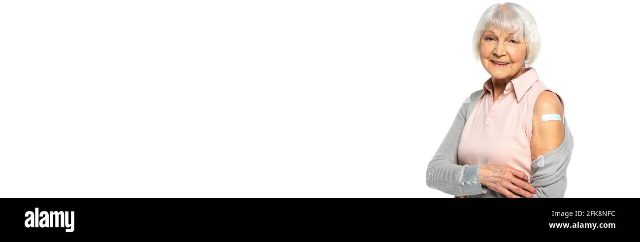 Ältere Frau mit Klebestreifen am Arm lächelt auf die Kamera isoliert auf weißem Banner Stockfoto
