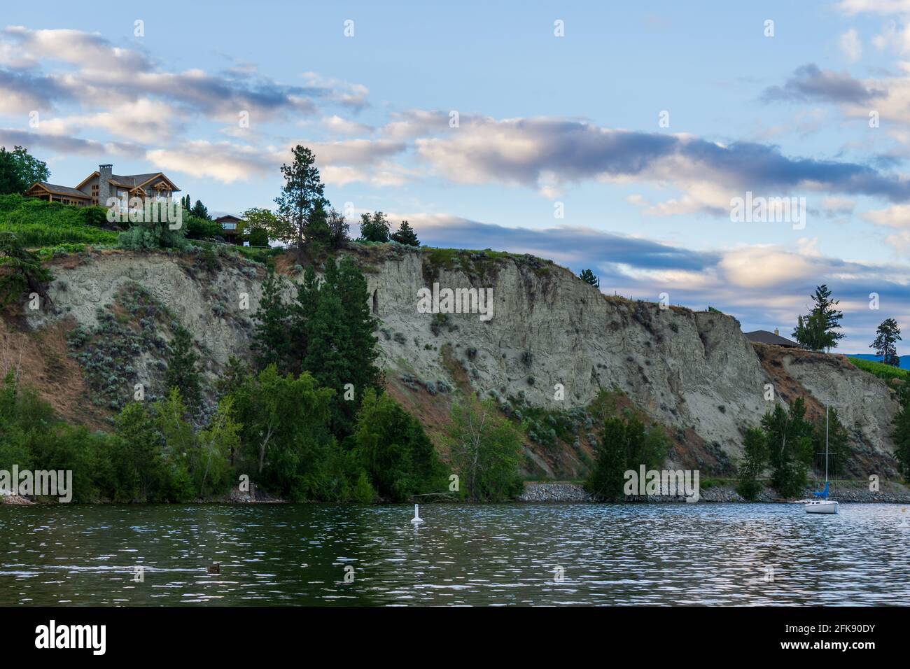 PENTICTON, KANADA - 04. JULI 2020: seenlandschaft mit Segelbooten ruhiger Morgen und Haus auf der Klippe. Stockfoto