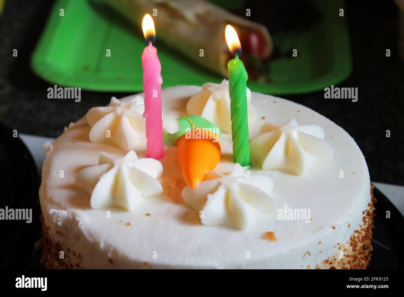 Nahaufnahme einer Karottenkuchen-Geburtstagstorte mit zwei Kerzen und einer orangefarbenen Puderkarotte darauf. Stockfoto
