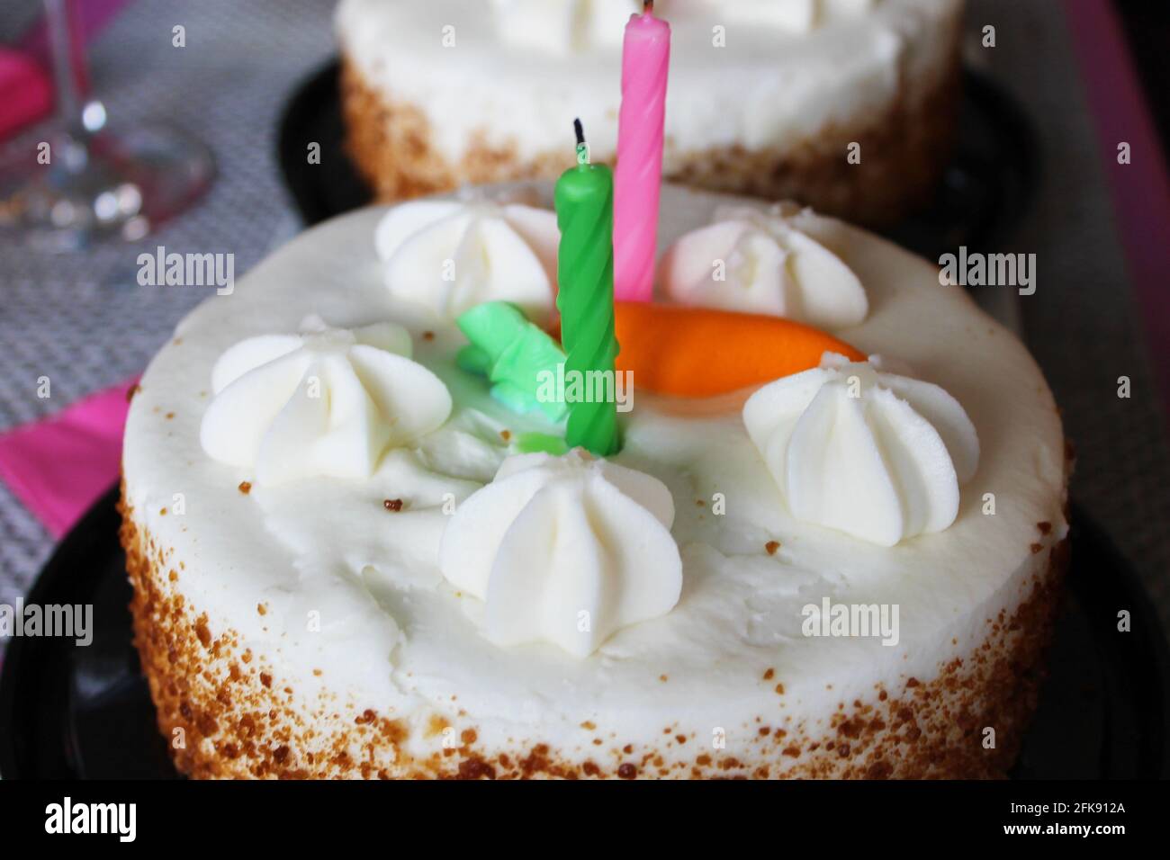 Nahaufnahme einer Karottenkuchen-Geburtstagstorte mit zwei Kerzen und einer orangefarbenen Puderkarotte darauf. Stockfoto