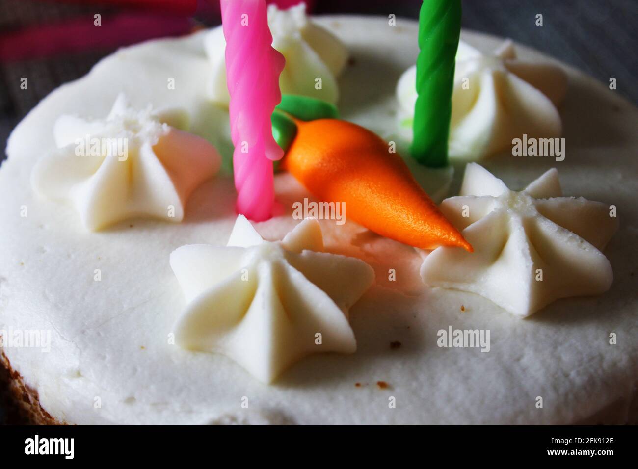 Nahaufnahme einer Karottenkuchen-Geburtstagstorte mit zwei Kerzen und einer orangefarbenen Puderkarotte darauf. Stockfoto