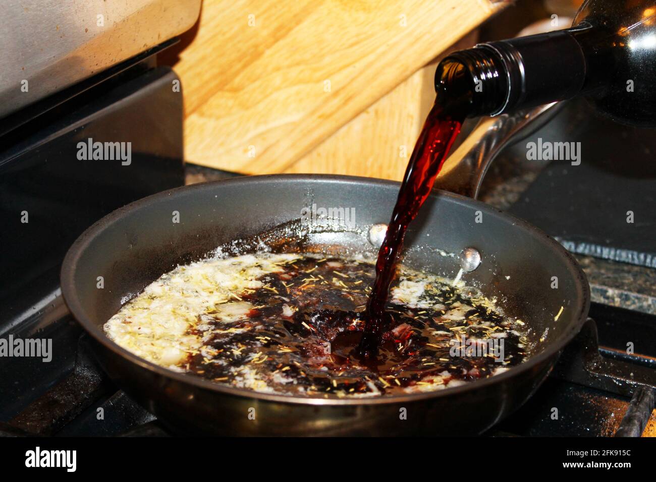 Nahaufnahme des Rotweins, der in eine Bratpfanne gegossen wird, um einen Rotwein und eine Schalotte-Sauce zu machen. Stockfoto