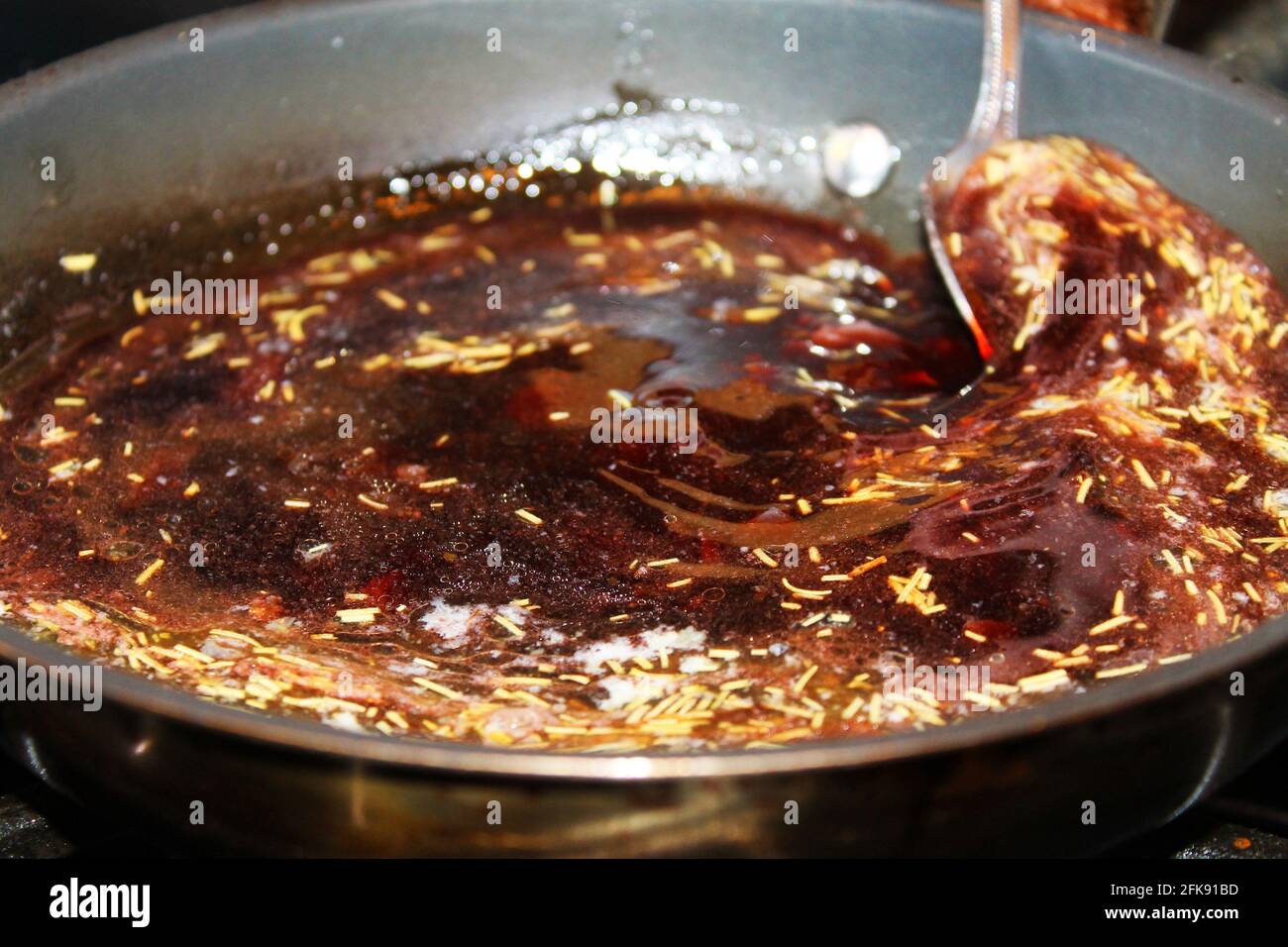 Nahaufnahme eines Rotweins und einer Schalotte-Sauce in einer Pfanne, die mit einem Löffel umgerührt wird. Stockfoto