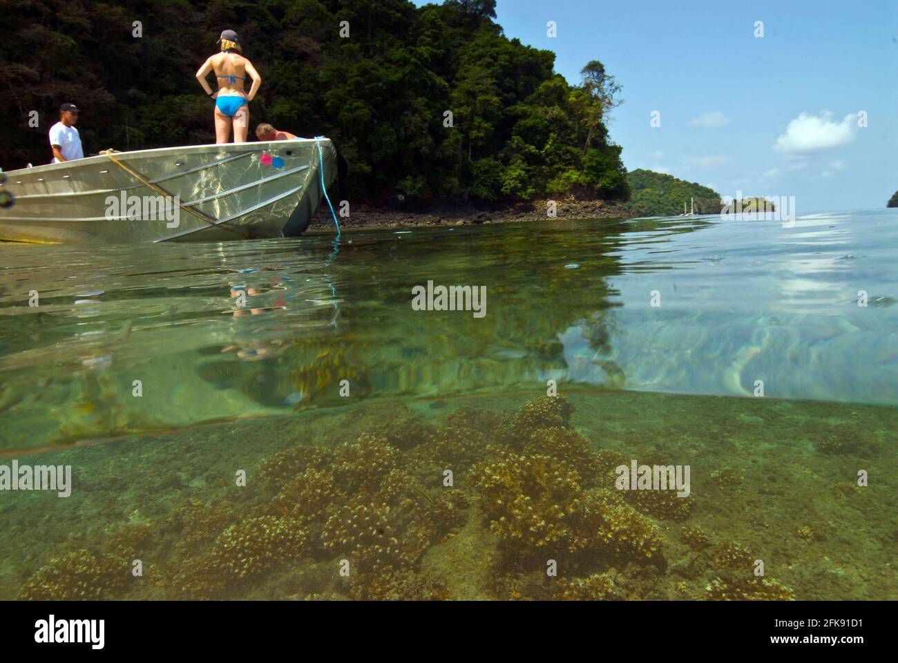 Über-unter-Foto von Menschen auf einem kleinen Boot, das über Hartkorallen in der seichten Lagune, Coiba Marine Park, Panama, verankert ist Stockfoto