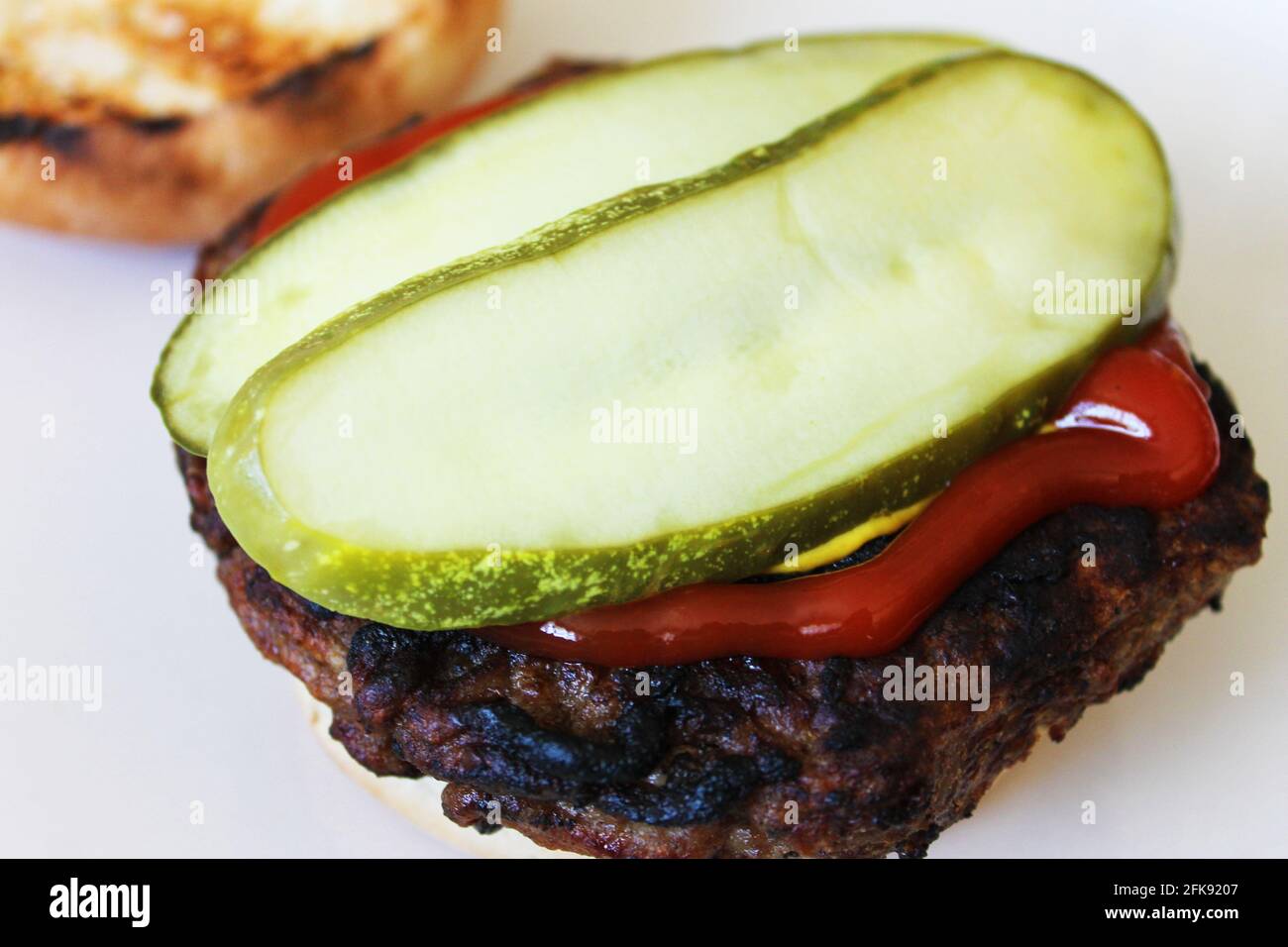 Nahaufnahme eines Hamburgers auf einem gerösteten Brötchen, bekleidet mit Ketchup, Senf und Dilleingelegter. Stockfoto