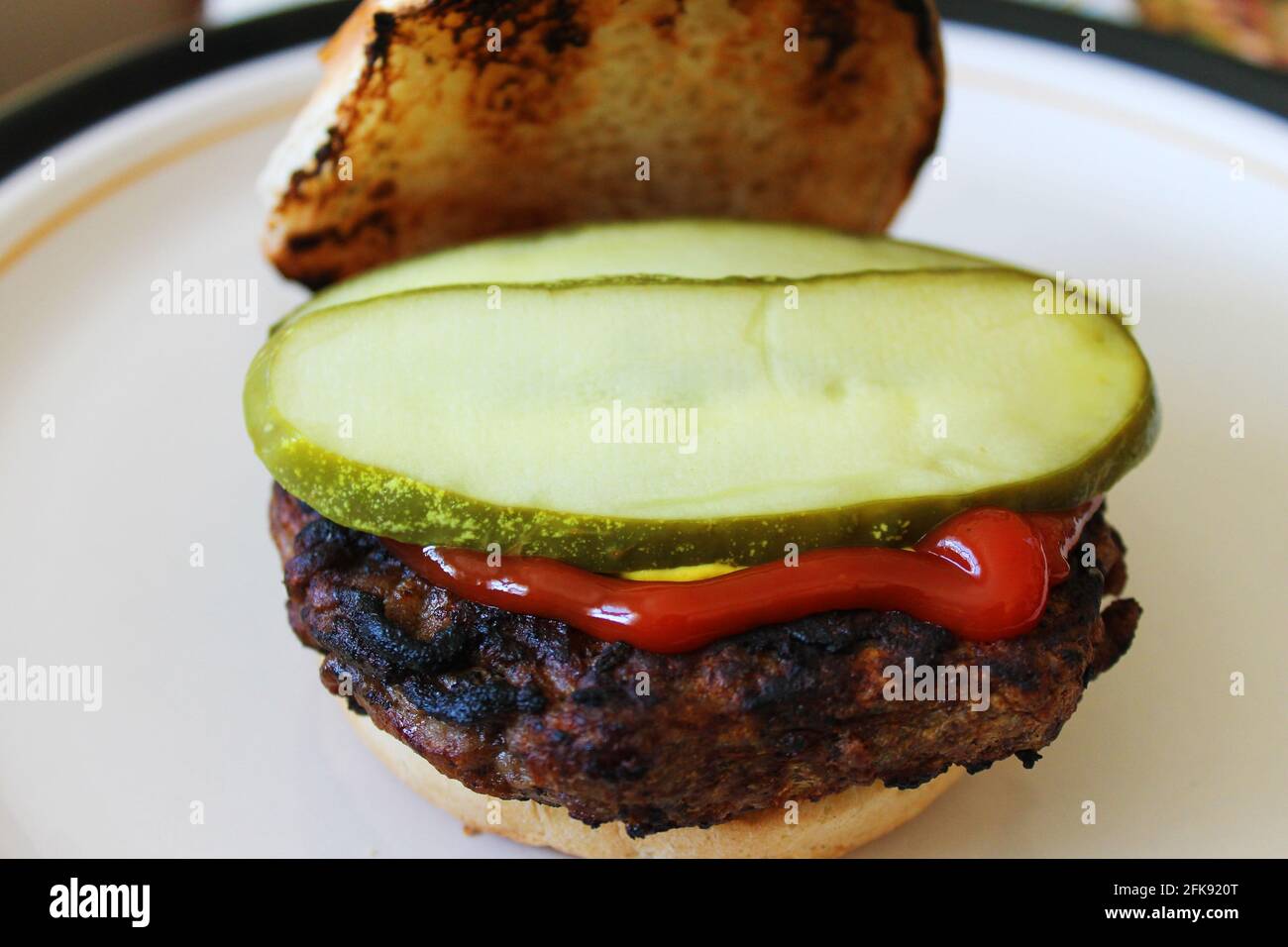 Nahaufnahme eines Hamburgers auf einem gerösteten Brötchen, bekleidet mit Ketchup, Senf und Dilleingelegter. Stockfoto