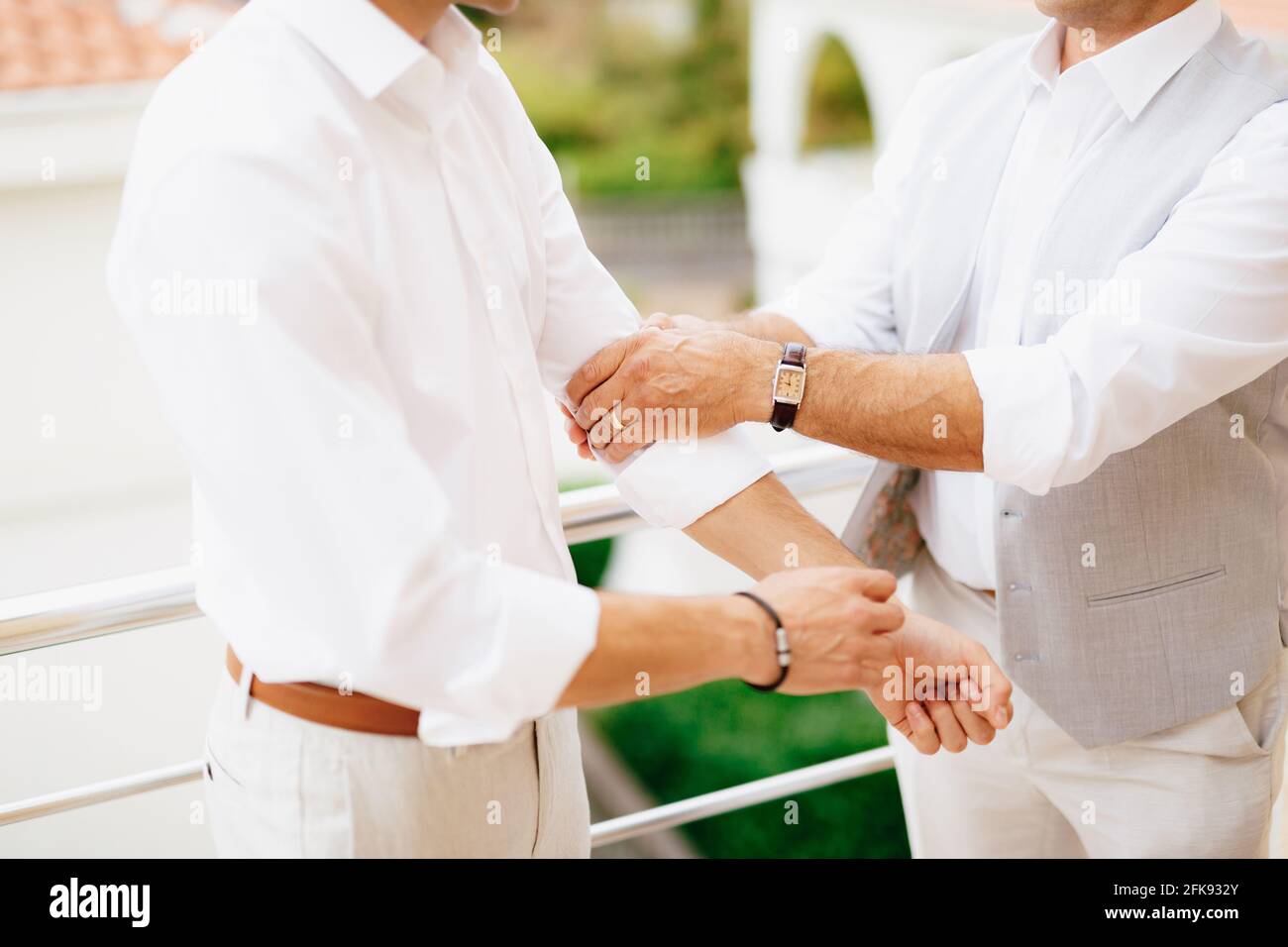 Der Bräutigam zieht die Ärmel seines Hemdes hoch, während er sich auf die Hochzeitszeremonie vorbereitet, der beste Mann hilft dem Bräutigam, sich vorzubereiten Stockfoto