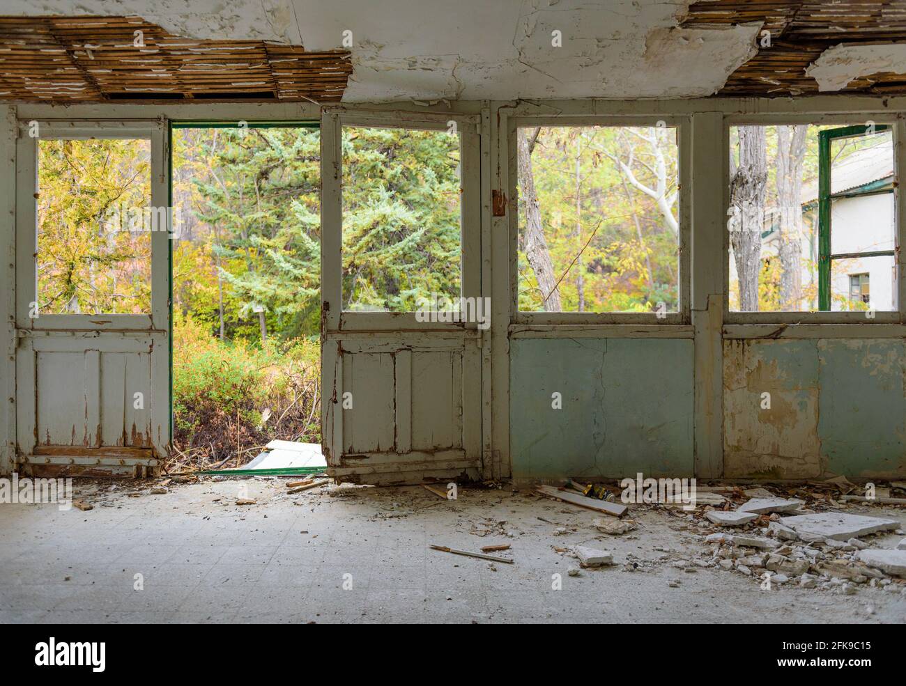 Verlassene Inneneinrichtung. Galerie mit Tür- und Fensterrahmen, zerbrochenem Glas und abgefallener Gips, überwucherter Herbstgarten durch die Fenster gesehen Stockfoto