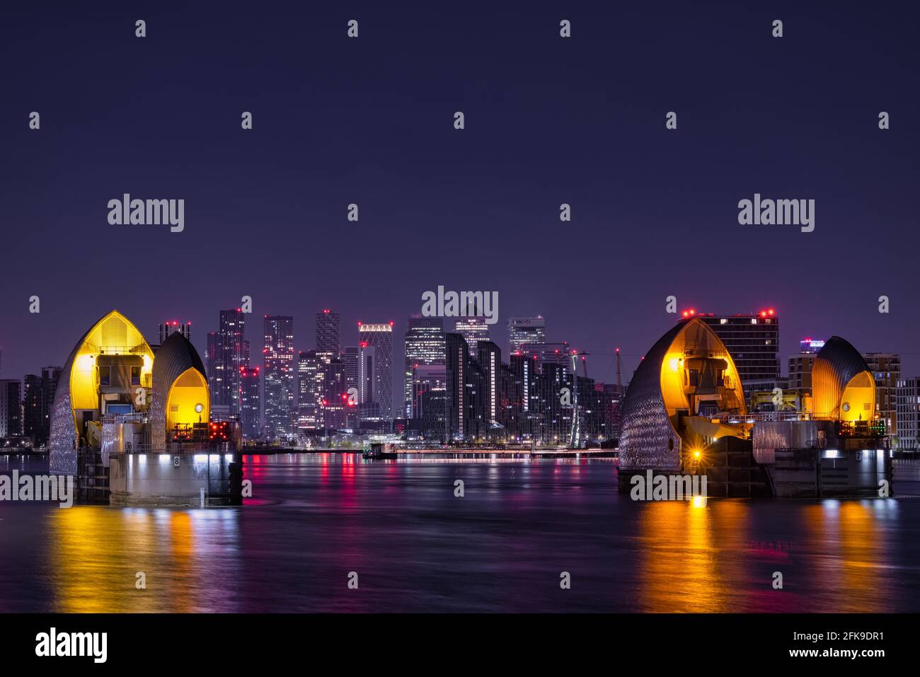 Die Thames Barrier bei Nacht mit der Isle of Dogs und Canary Wharf im Hintergrund. Stockfoto