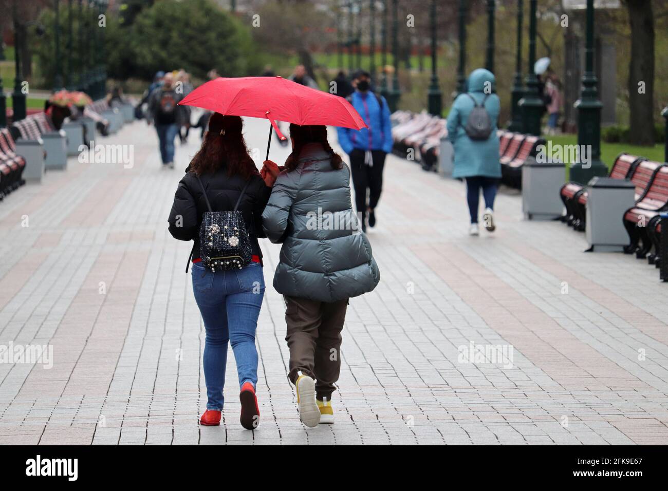 Regen in der Stadt, zwei Mädchen mit einem Regenschirm gehen auf einer Straße vor dem Hintergrund der Menschen. Regnerisches Wetter, Frühlingssturm Stockfoto