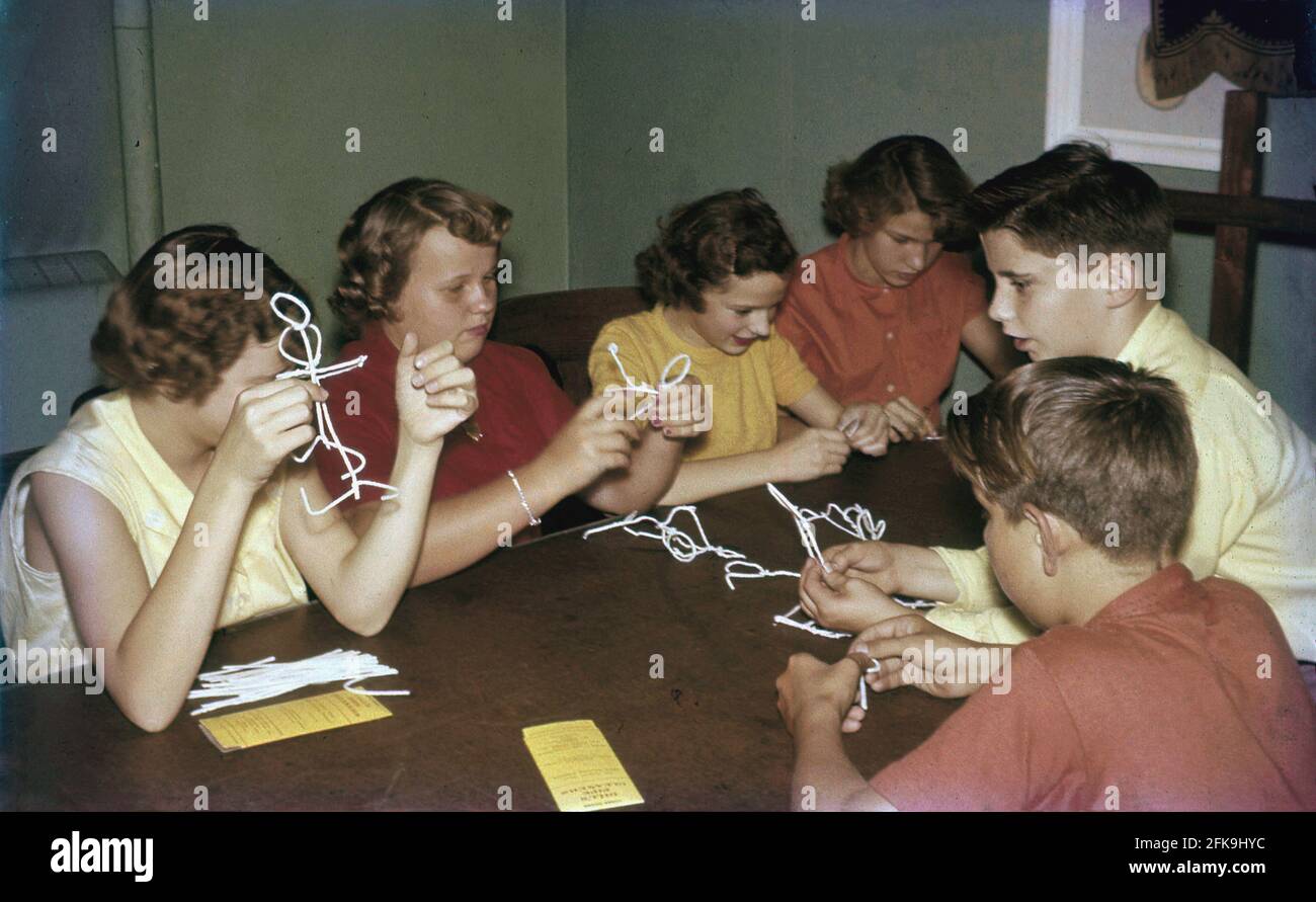 1960er Jahre, historisch, in einem Raum, mehrere Jungen und Mädchen, sitzen an einem Tisch spielen mit schlichten weißen Pfeifenreiniger, whch sie sich in Formen biegen, um Stick Men Figuren oder Tierskulpturen zu machen. Ein Pfeifenreiniger ist eine kleine dünne Bürste, die ursprünglich zum Entfernen von Rückständen von rauchenden Rohren bestimmt war, aber aufgrund ihrer Flexibilität hervorragend für Kinder in Kunst- und Bastelprojekten geeignet ist, um mit zu spielen und aus denen Formen und Figuren gemacht werden können. Es wurde zu einer beliebten Pasttime für Kinder in dieser Zeit und bleibt so heute, wie es Einfachheit ermöglicht Phantasie und Kreativität. In Japan ist es als Mogol Art bekannt. Stockfoto