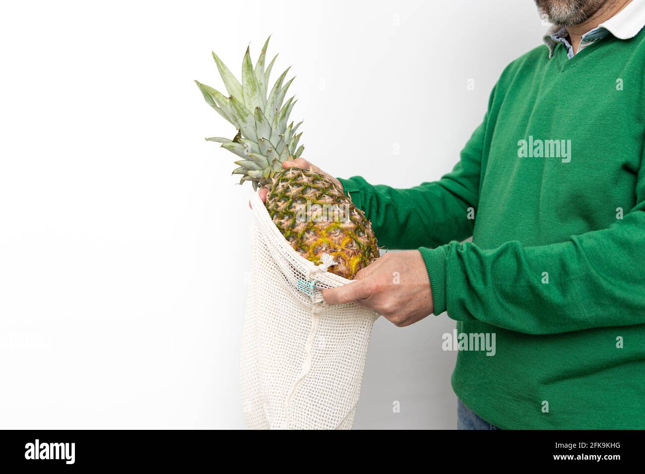 Erwachsenes Männchen, das eine Ananas in ein Fruchtnetz legt. Speicherplatz kopieren. Weißer Hintergrund. Stockfoto