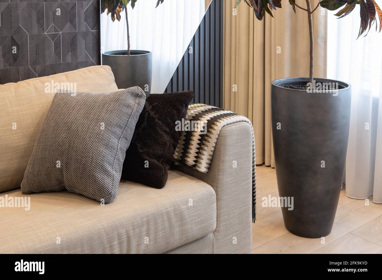 Die Inneneinrichtung des Wohnzimmers in neutralen Erdtönen. Großes Sofa mit dekorativen Kissen, Topfpflanze Croton, geometrischer Holzplatte und Spiegel an der Wand. Co Stockfoto