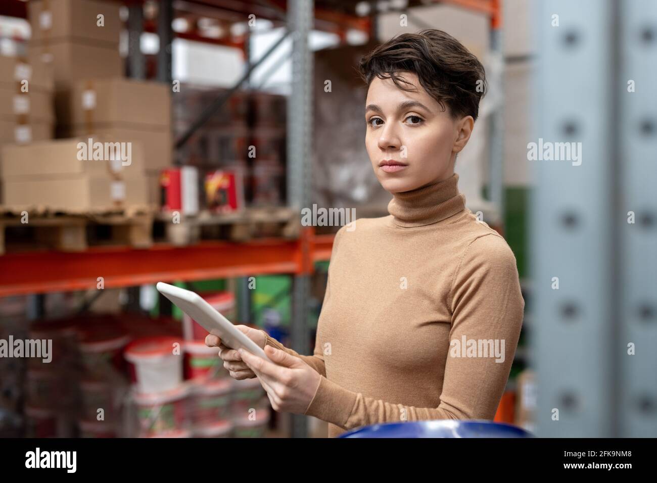 Porträt eines ernsthaften Supply Managers mit braunem Haar, gegen das man sich wenden kann Lagerrahmen und Arbeiten mit Daten auf dem Tablet Stockfoto