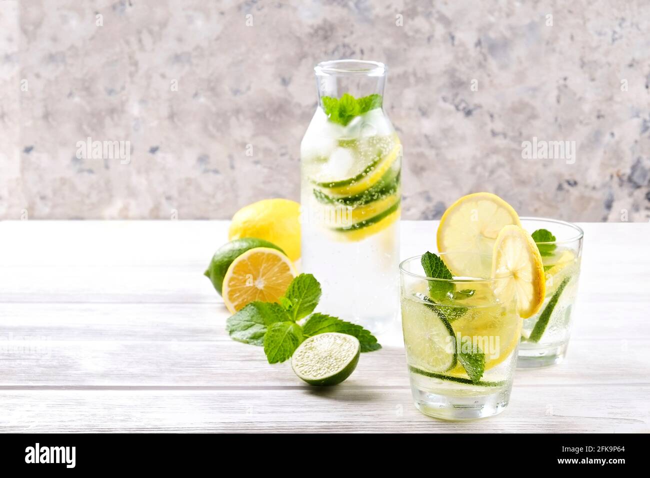 Vintage-Flasche mit zwei Gläsern erfrischendem alkoholfreien Mojito Limonade-Getränk mit Zitrone, Limettenscheiben, Minzblättern, Stroh, Eis auf Holztisch, CO Stockfoto