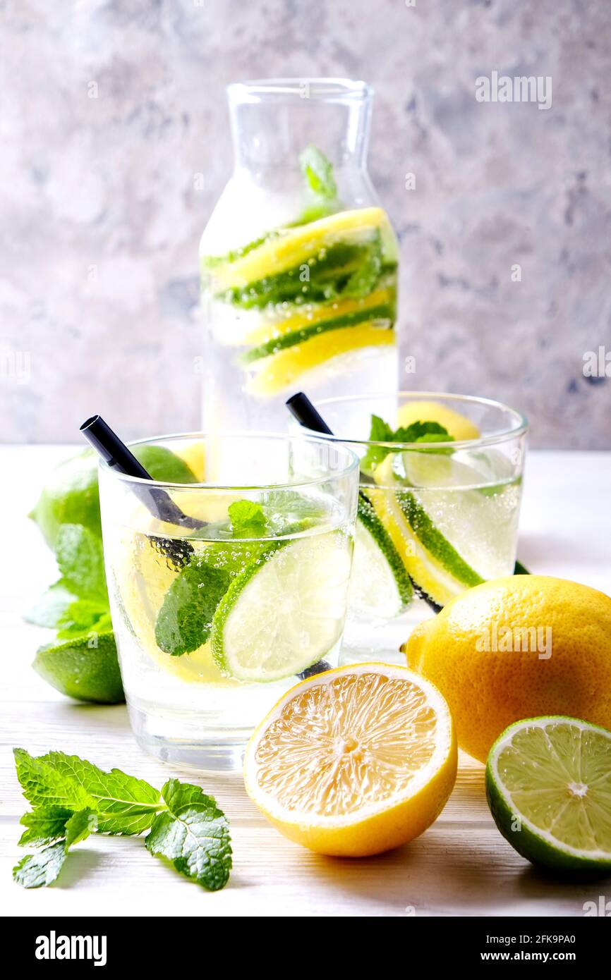 Vintage-Flasche mit zwei Gläsern erfrischendem alkoholfreien Mojito Limonade-Getränk mit Zitrone, Limettenscheiben, Minzblättern, Stroh, Eis auf Holztisch, CO Stockfoto