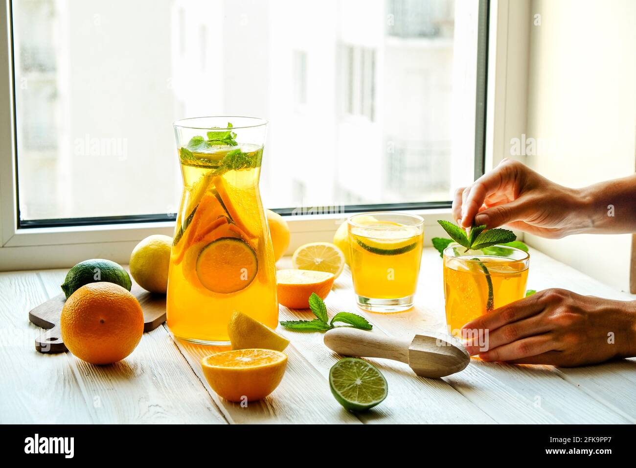 Nahaufnahme der Hände einer jungen Frau, die frische Limonade herstellte, Saft aus Zitrusfrüchten drückte, Entsafter. Krug voll mit kaltem Getränk mit Zitrone, Orange, l Stockfoto