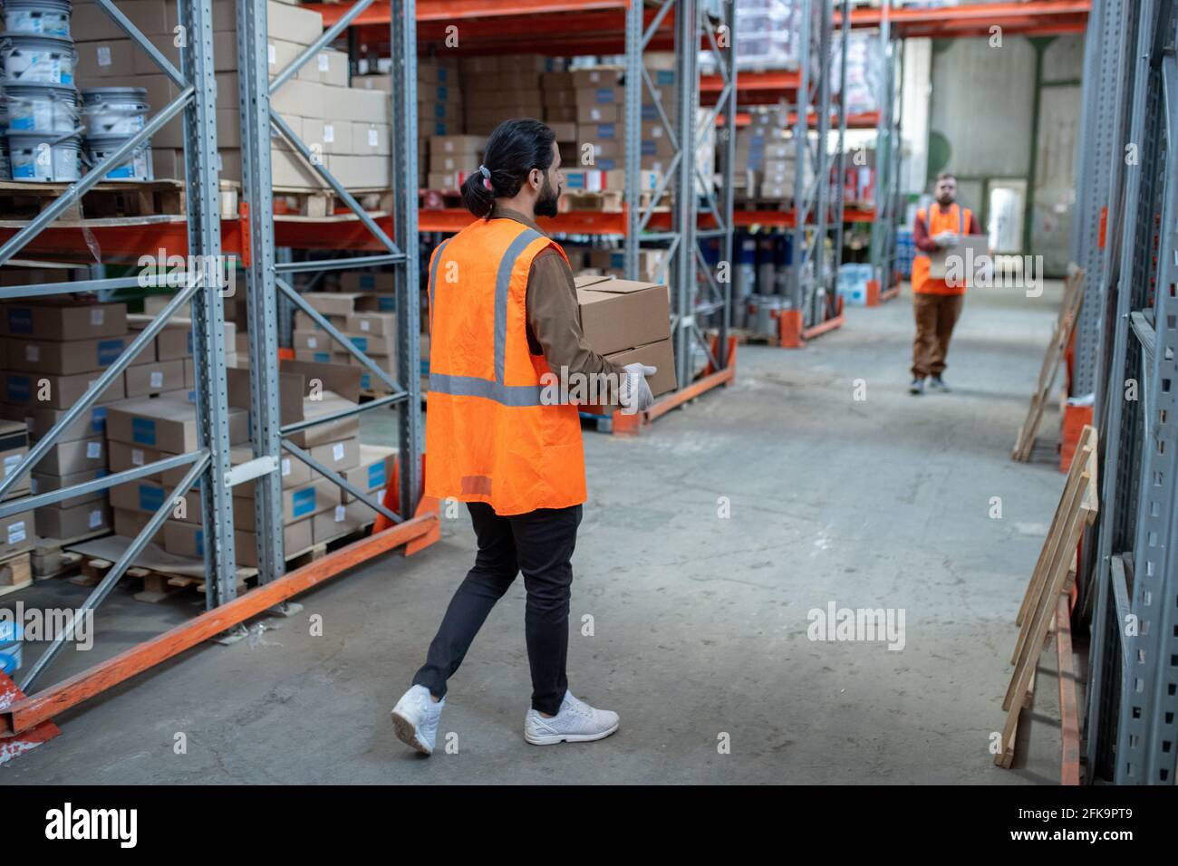 Lagerarbeiter in reflektierenden Westen bewegen Kisten, während sie Artikel verteilen Im Lagerraum mit Metallregalen Stockfoto