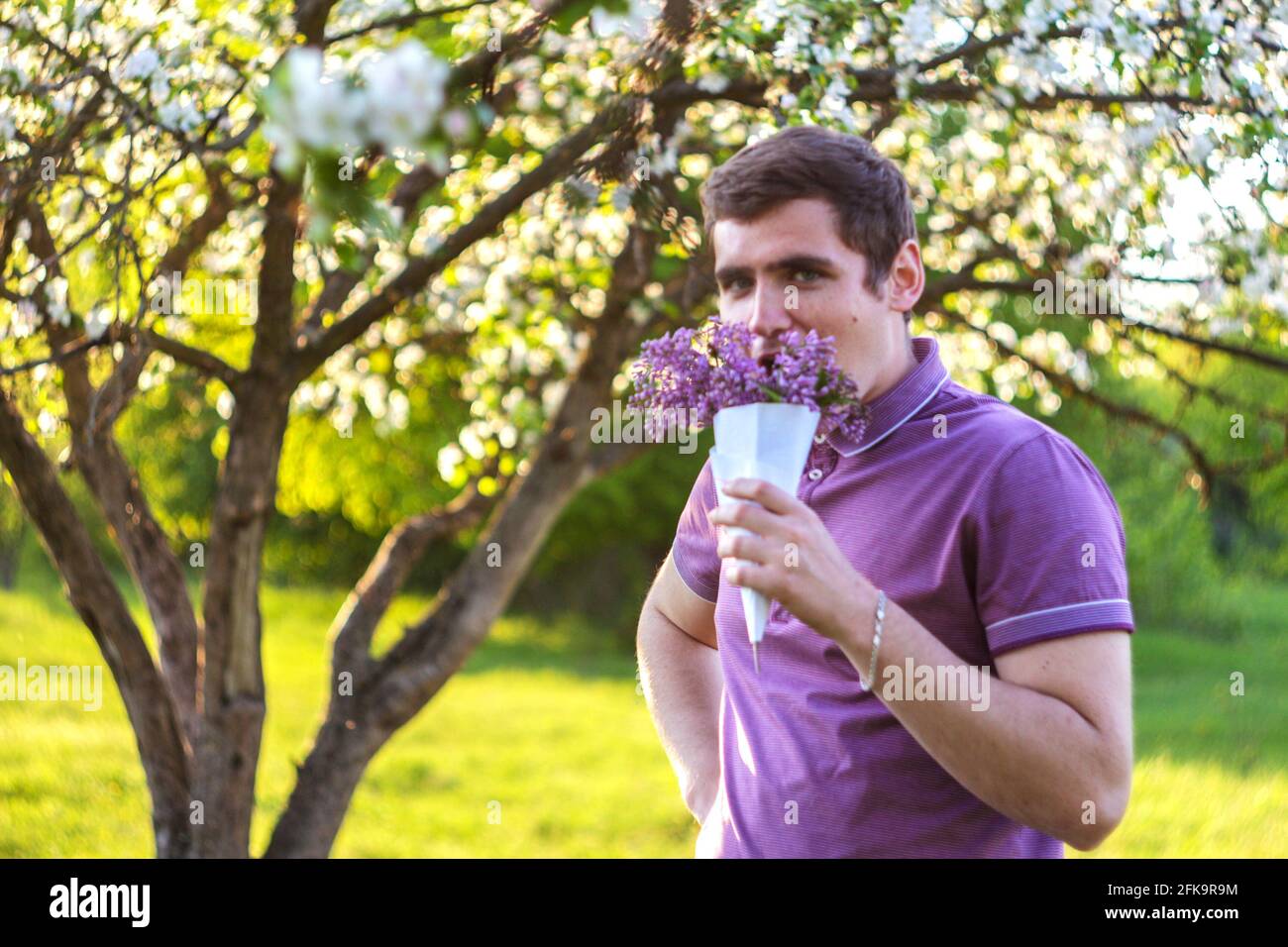 Unschärfe-Porträt eines hübschen kaukasischen Mannes mit Kegelblumen in Flieder Garten Lustige Freude junge Brünette Kerl riecht frische Blumen Und betrachten Stockfoto