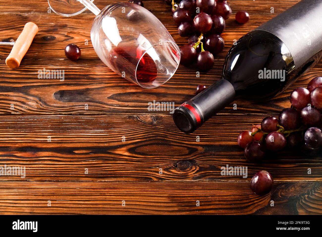 Vintage Flasche Rotwein mit leerem mattschwarzes Etikett, gegossenes Glas, Korkenzieher & Trauben, grunged Holztisch Hintergrund. Teure Flasche cabernet Stockfoto