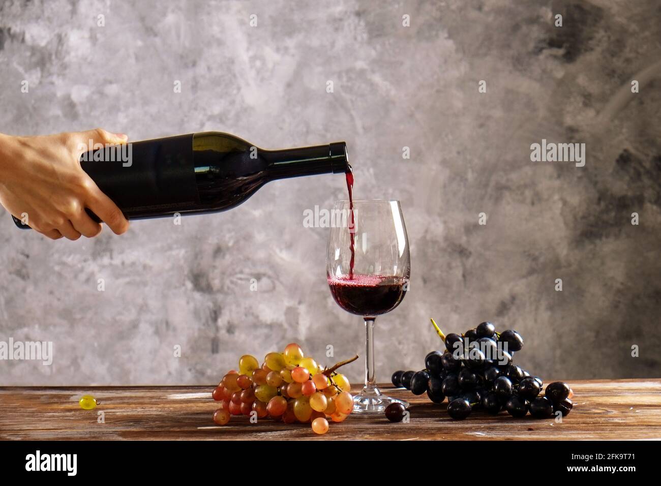 Frau, die eine Flasche Rotwein hält. Nahaufnahme einer jungen weiblichen Hand, die teuren cabernet-Sauvignion in einen Glastisch aus Holz gießt. Verschiedene Buns Stockfoto