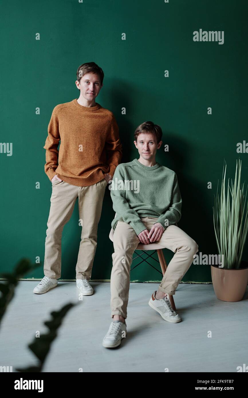 Content-Portrait junge Zwillinge in hellen Pullovern und Beige Lässige Hose, die gegen die grüne Wand posiert Stockfoto