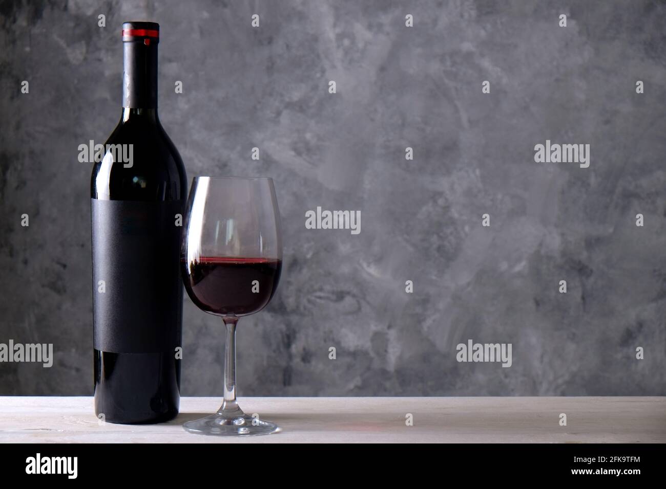 Vintage Flasche Rotwein mit leerem mattschwarzes Etikett, Trauben auf Holztisch, Betonwand Hintergrund. Teure Flasche cabernet sauvi Stockfoto